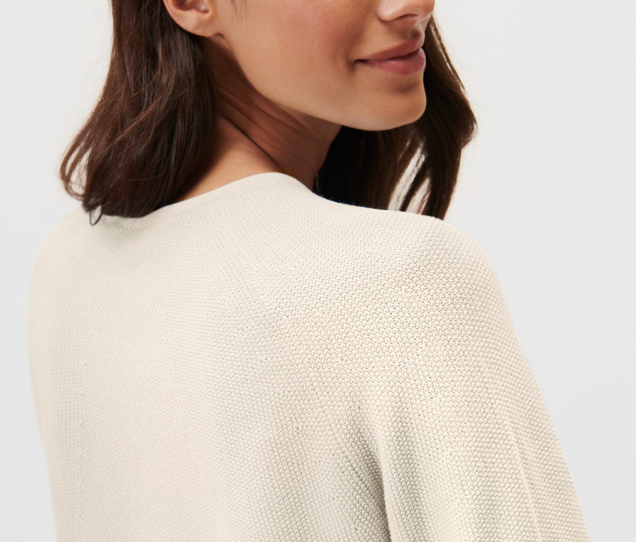 Žena má na sebe pletený pulóver krémovej farby.
