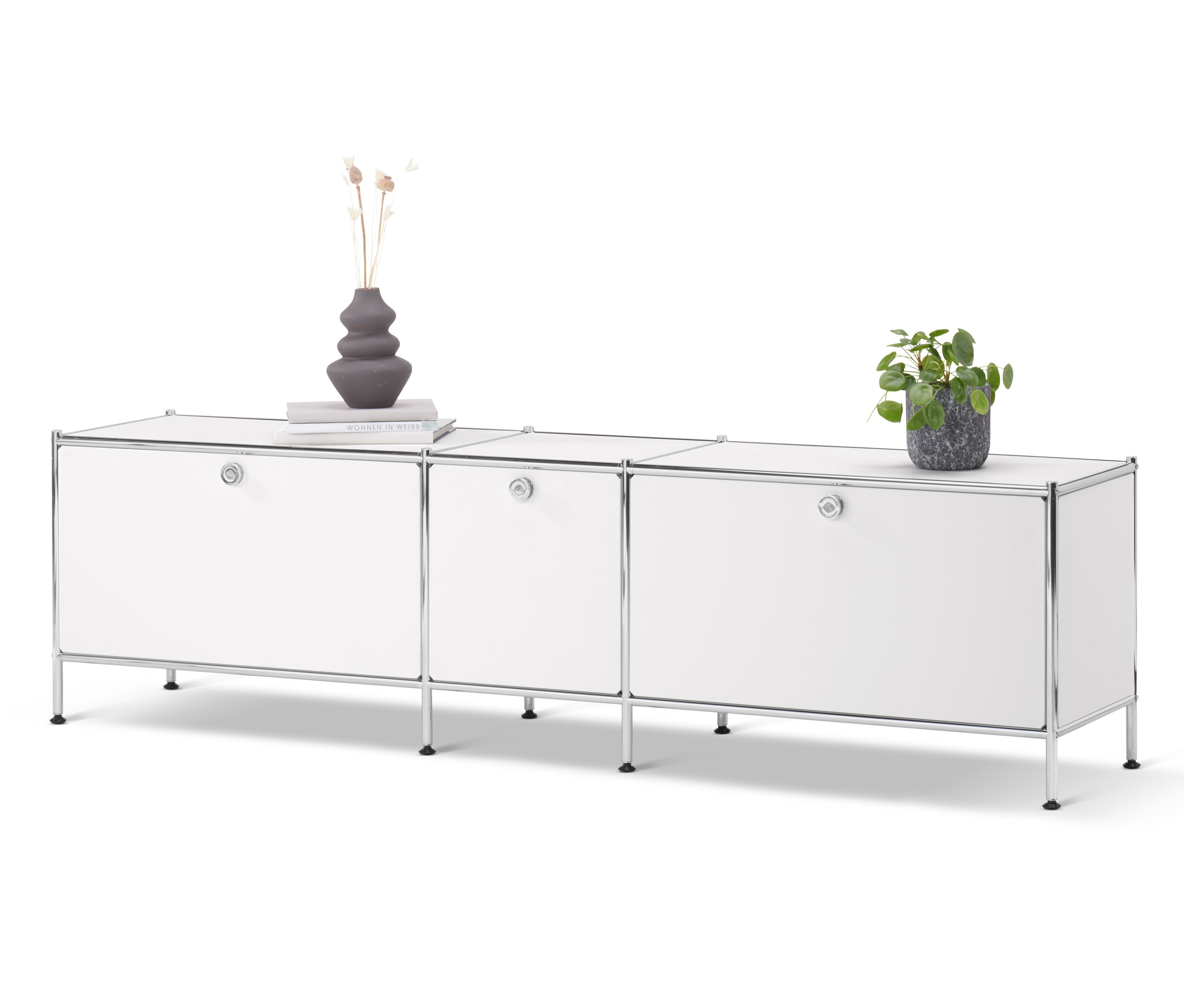 Biela nízka skrinka »CN3« s 3 výklopnými dvierkami. Na skrinke váza, kniha a kvetina v kvetináči.