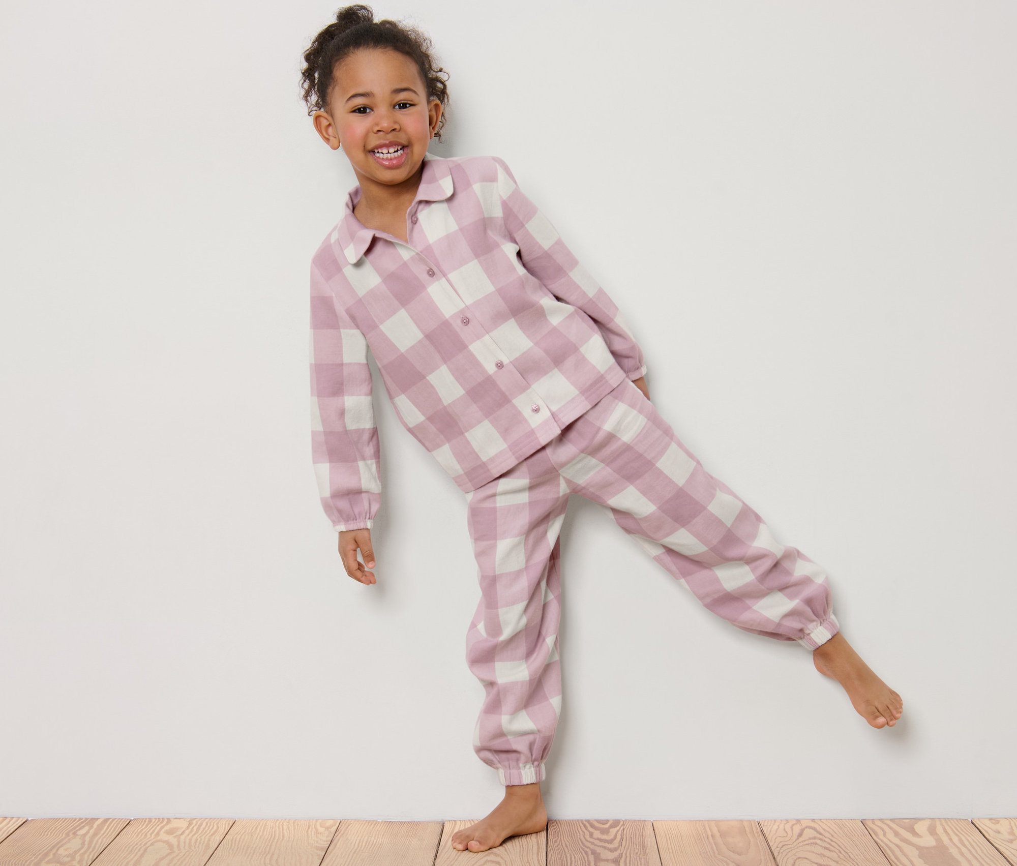 Usmievajúce sa dievčatko pózuje v detskom flanelovom pyžame s kockovaným vzorom.
