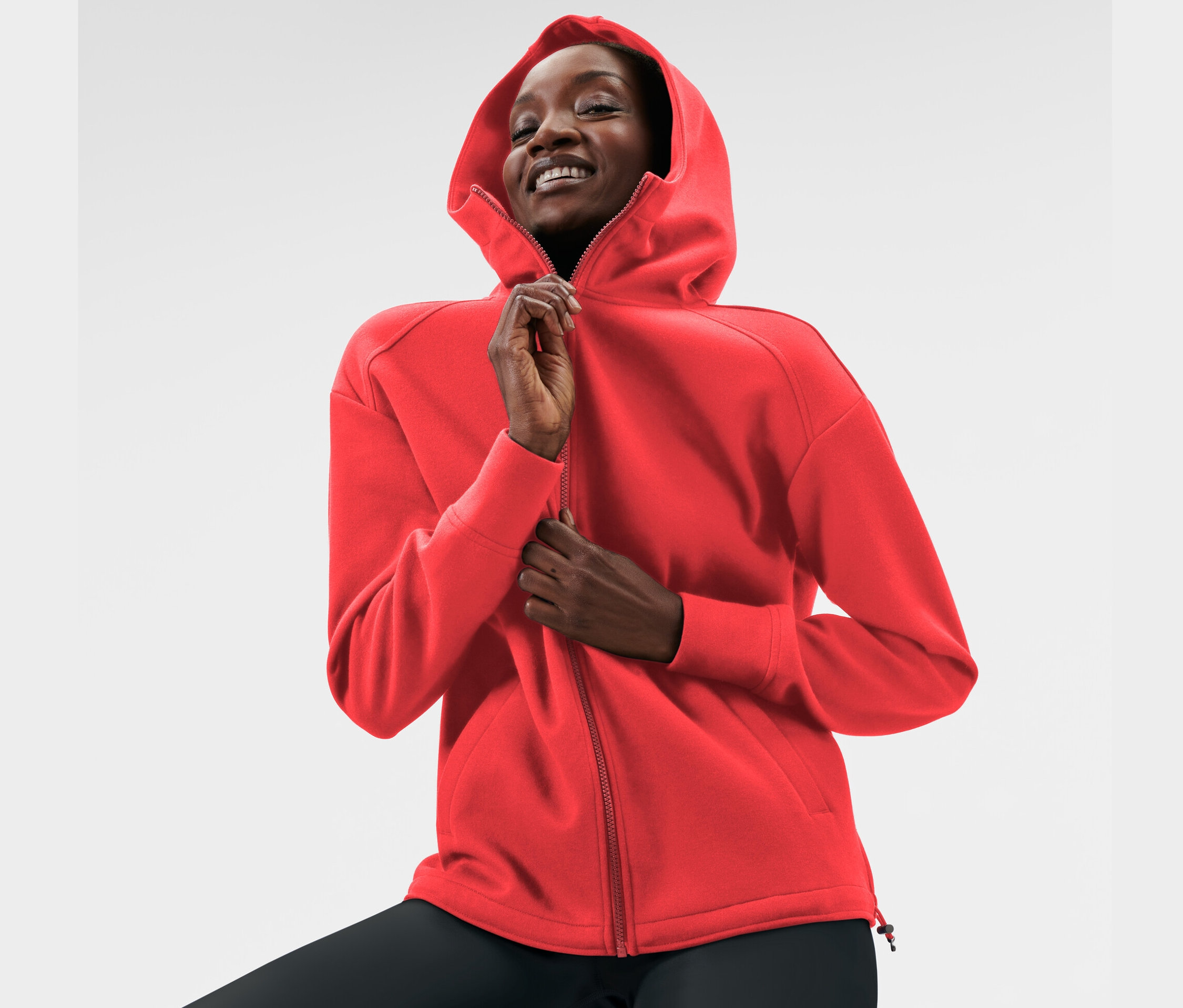 Žena si zapína červenú mikinu s kapucňou.