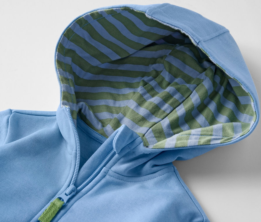 Detail modrej detskej mikiny s kapucňou s vnútornou stranou s modrými a zelenými pruhmi a zipsom.
