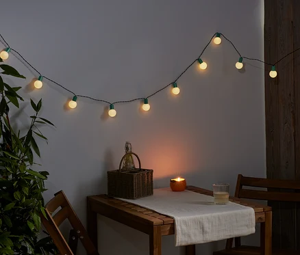 Na stene visí svetelná reťaz s LED. Na stole stojí košík, sviečka a pohár.