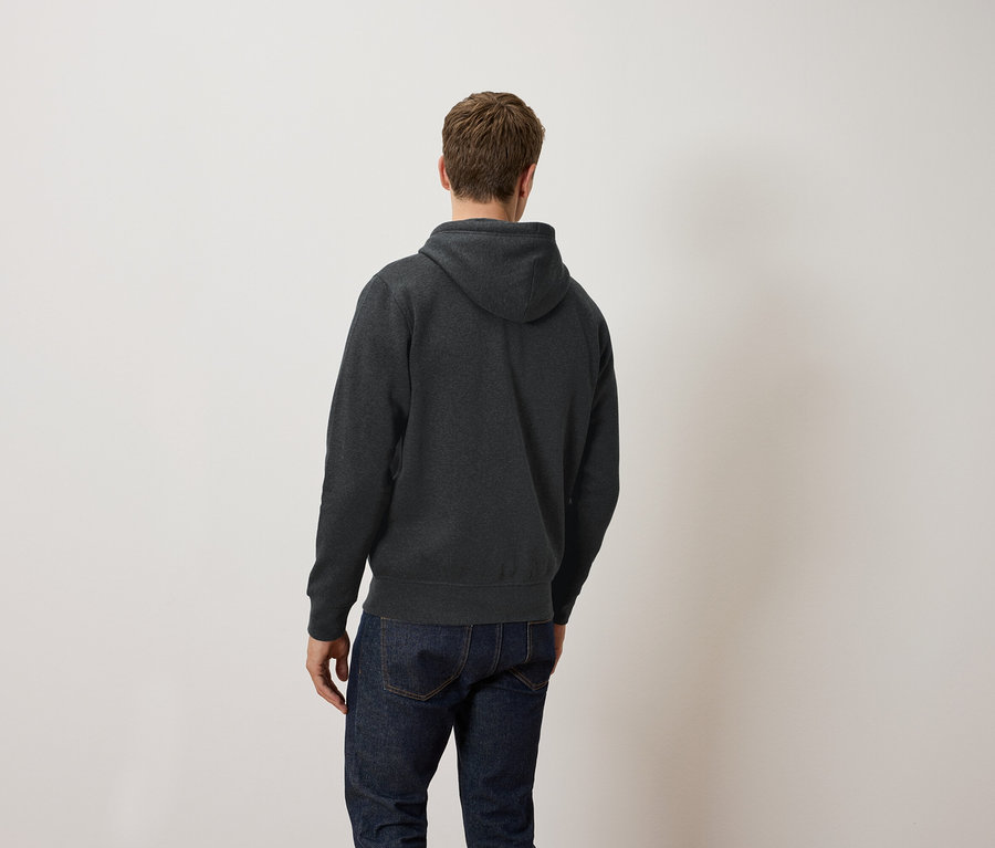 Muž chrbtom k fotoaparátu má na sebe tmavosivú mikinu s kapucňou a džínsy.