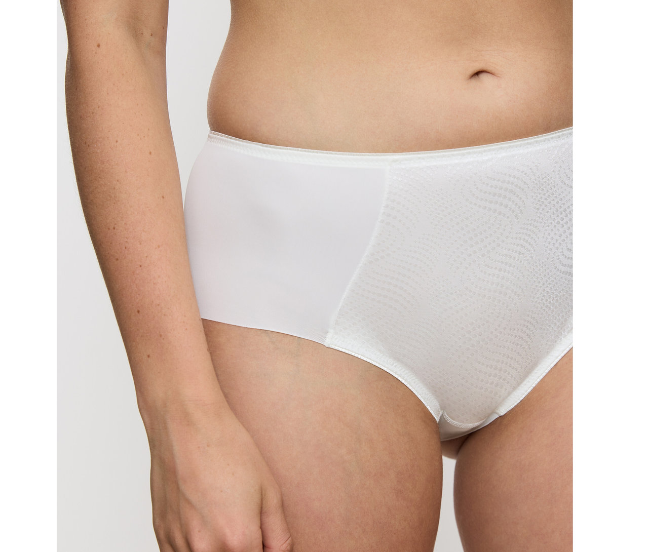 Zblízka osoba v vanilkových nohavičkách Triumph Essential »Minimizer Hipster X«. Nohavičky majú na prednej strane štruktúrovaný vlnitý vzor.