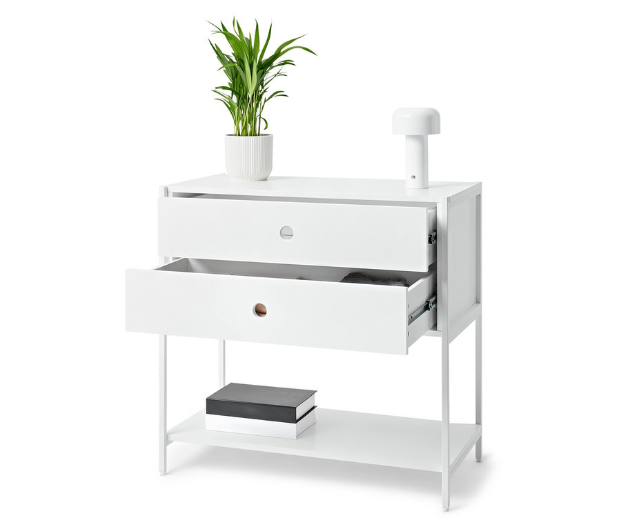 Biely stolík s dvoma zásuvkami, z ktorých jedna je otvorená, na ktorom stojí rastlina v kvetináči a lampa. Na spodnej polici ležia knihy.