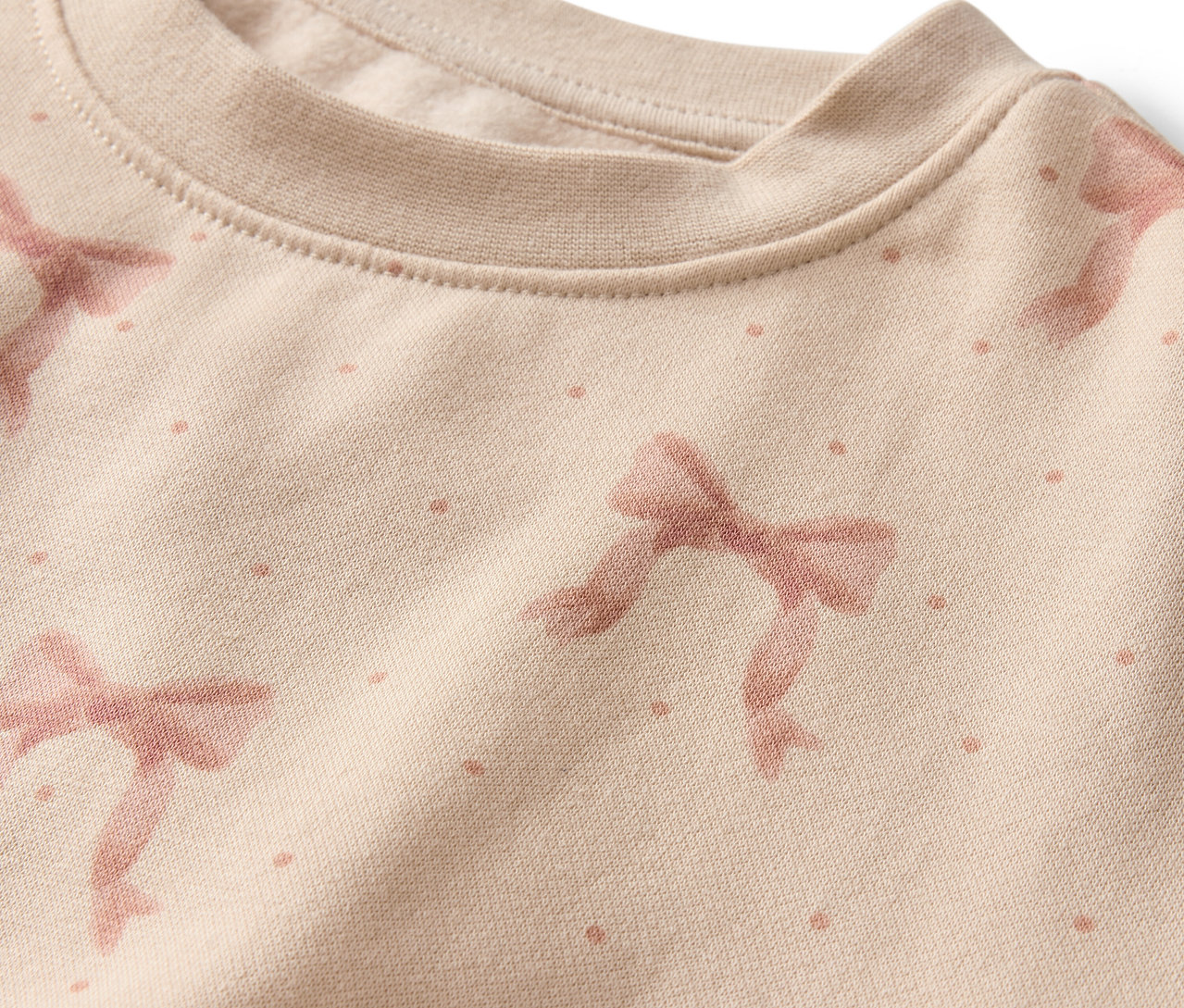 Detail béžovej mikiny s potlačou ružových mašlí a bodiek.