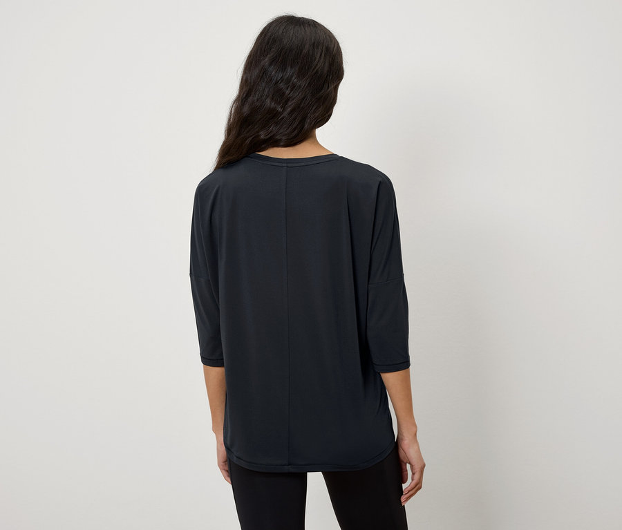 Žena chrbtom k fotoaparátu má na sebe čierne tričko s trojštvrťovými rukávmi.