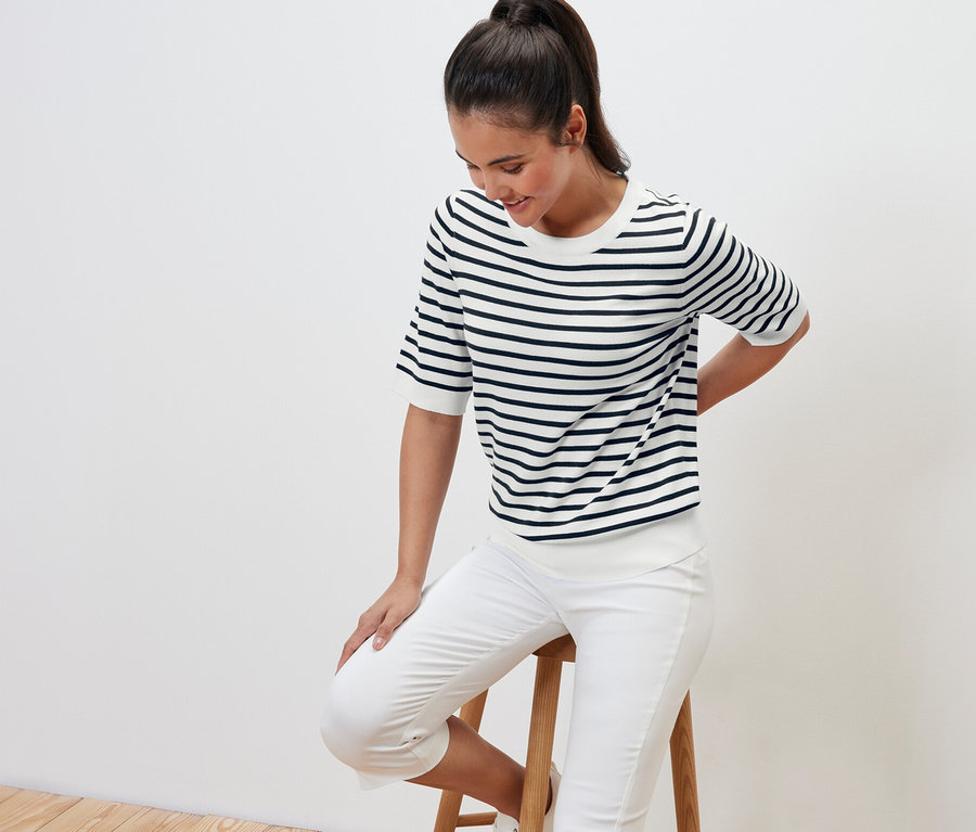 Žena sedí na stoličke a má na sebe tmavomodrý pruhovaný pulóver z jemného úpletu.