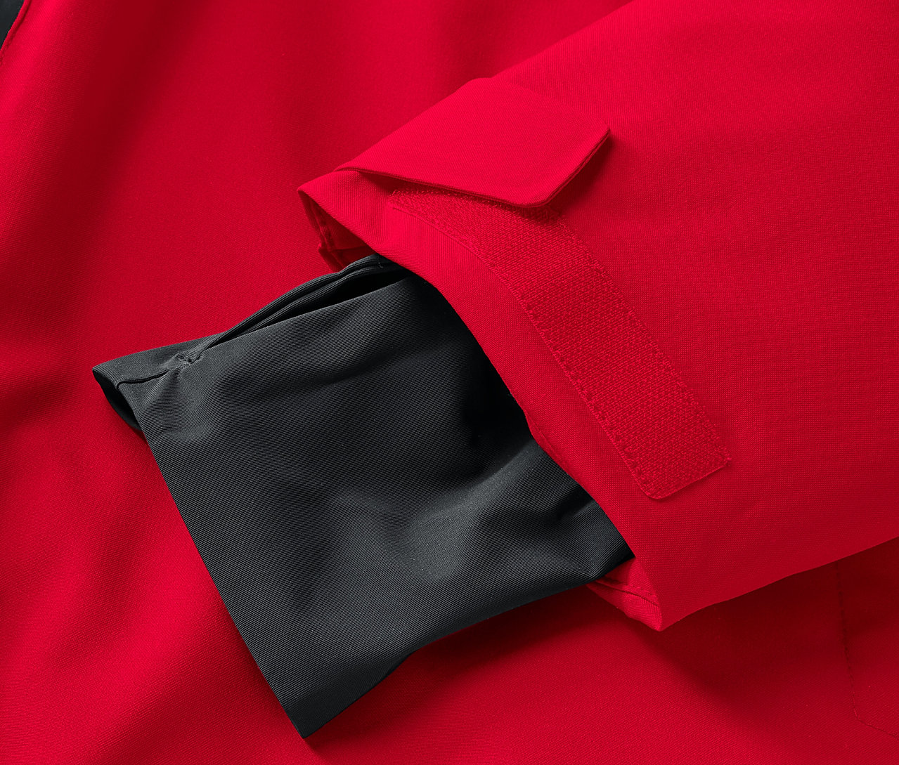 Detail červenej bundy s čiernym vnútorným vreckom na rukáve.