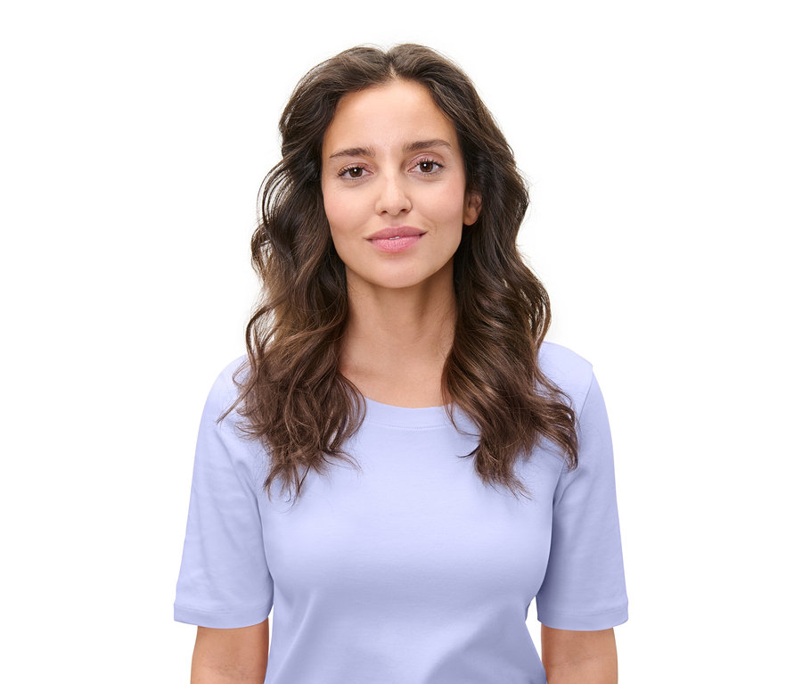 Portrét ženy s hnedými vlnitými vlasmi a svetlomodrým tričkom na bielom pozadí.