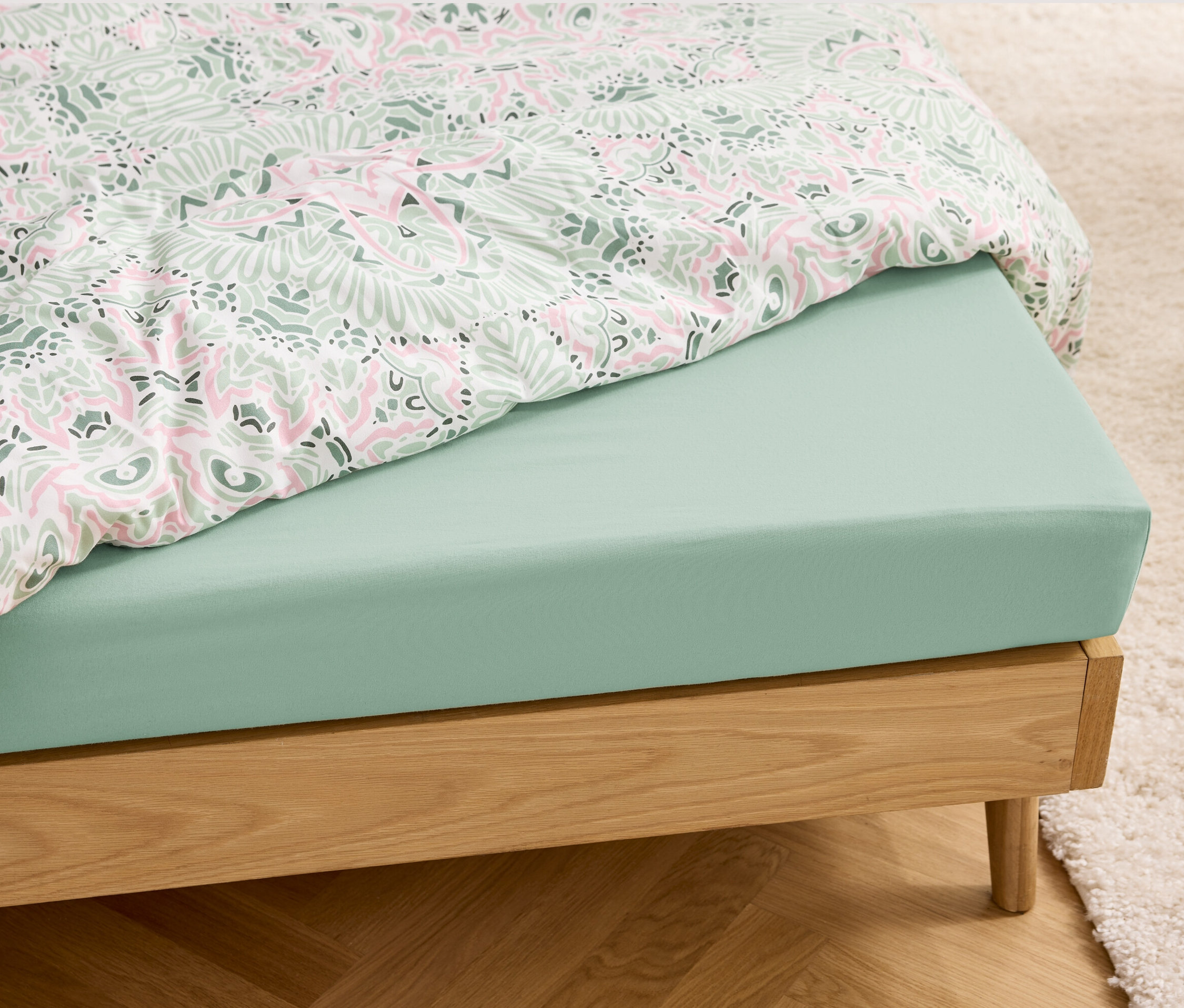 Svetlozelená džersejová plachta na posteli s dreveným rámom.