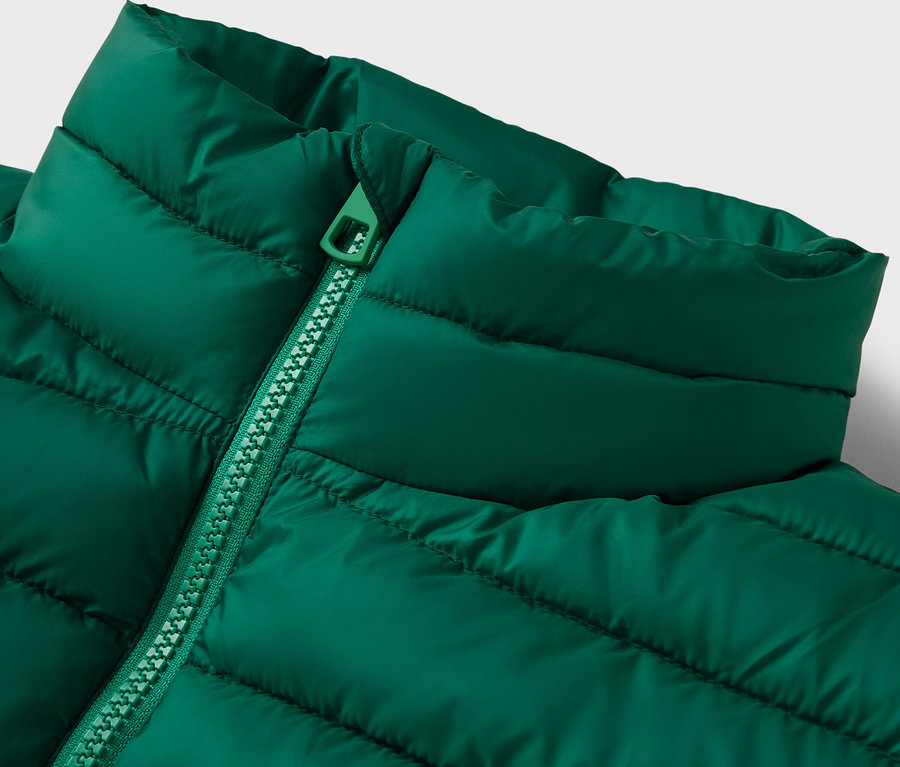 Detail zelenej prešívanej bundy s golierom a zipsom.