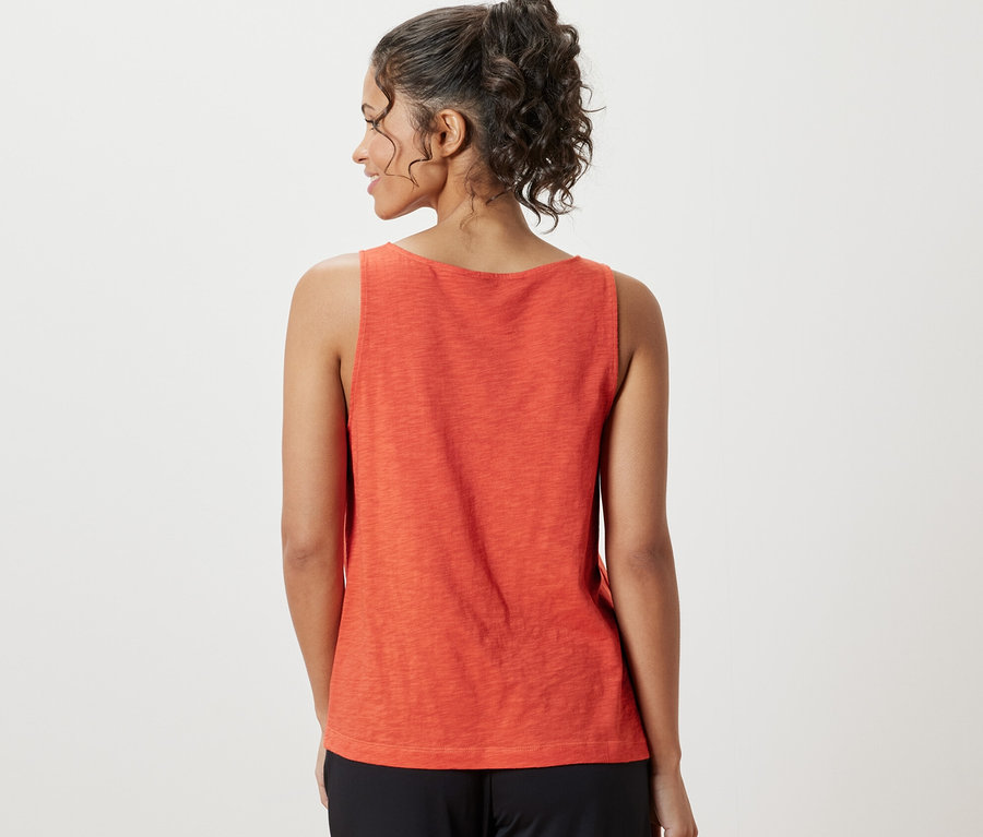 Žena má na sebe oranžový top z modalovej zmesi a čierne nohavice.