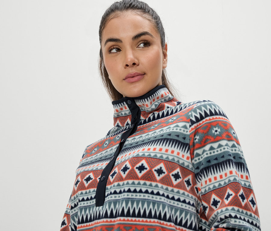 Portrét ženy s hnedými vlasmi v pestrofarebnej fleecovej mikine s geometrickým vzorom.