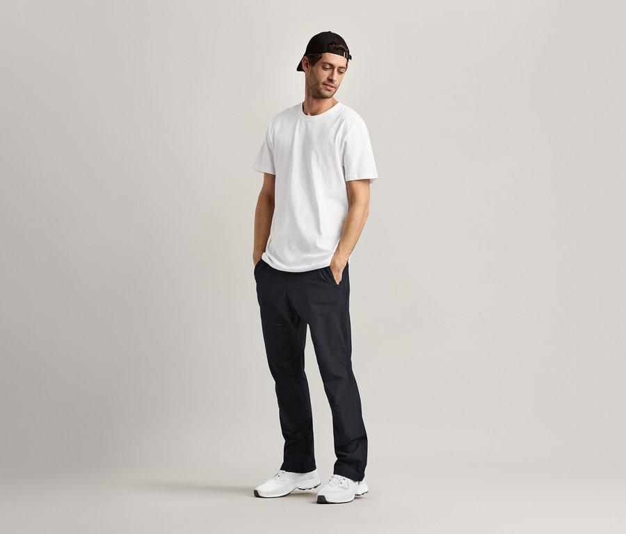 Muž stojí s rukami vo vreckách a má na sebe 2 tričká s okrúhlym výstrihom, biele.