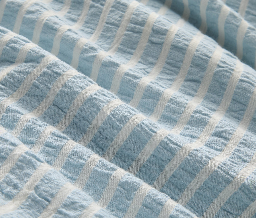 Detail záberu svetlomodrej látky s bielymi pruhmi a záhybmi.