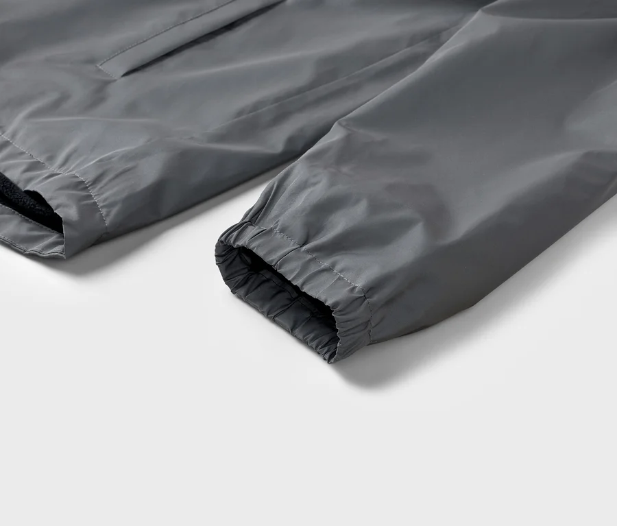 Detailný záber sivého rukáva bundy s elastickou manžetou na bielom pozadí.