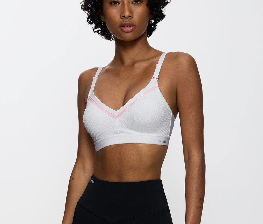Žena má na sebe bielu športovú podprsenku s ružovými detailmi a čierne legíny.