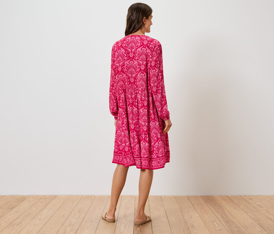 Pohľad zozadu na ženu v ružových šatách po kolená s kvetinovým vzorom a sandálmi.