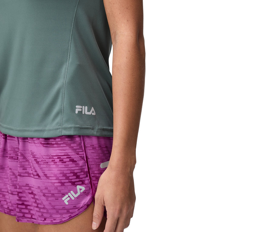 Detail ženy v zelenom tope Fila a fialových šortkách.