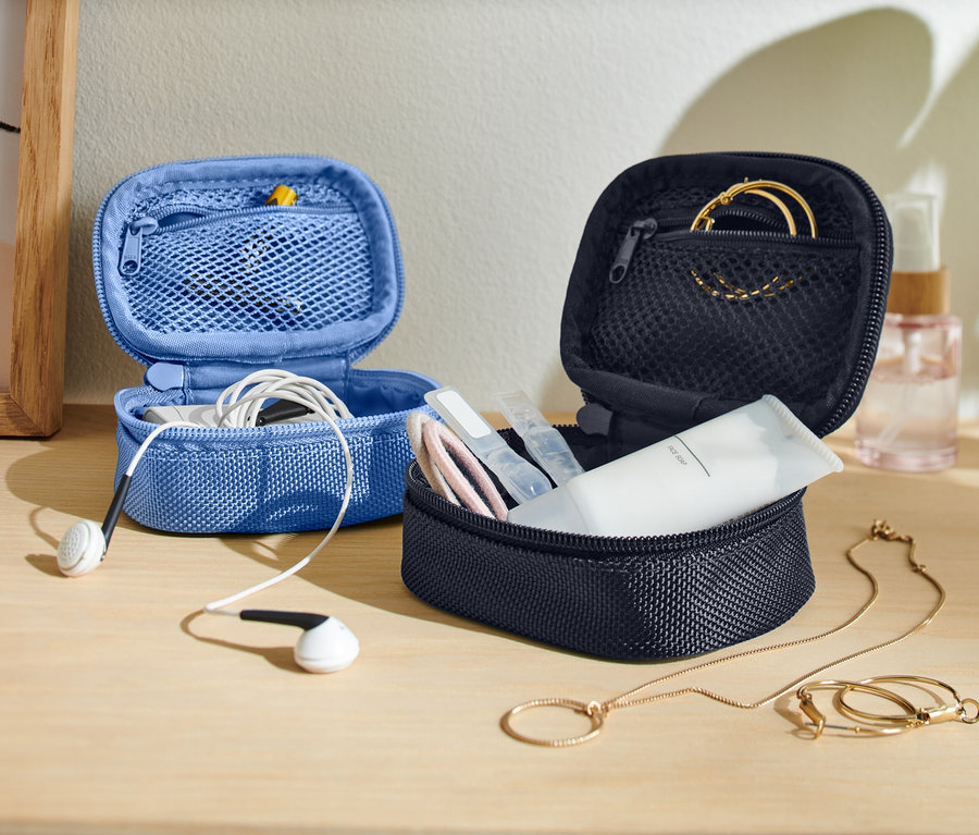 Na stole sú dve otvorené, malé úložné tašky, jedna modrá so slúchadlami a jedna tmavá s produktmi starostlivosti o pleť a šperkami.
