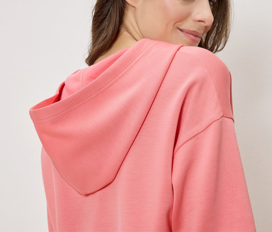 Žena má na sebe lososovú mikinu s kapucňou, pohľad zboku.