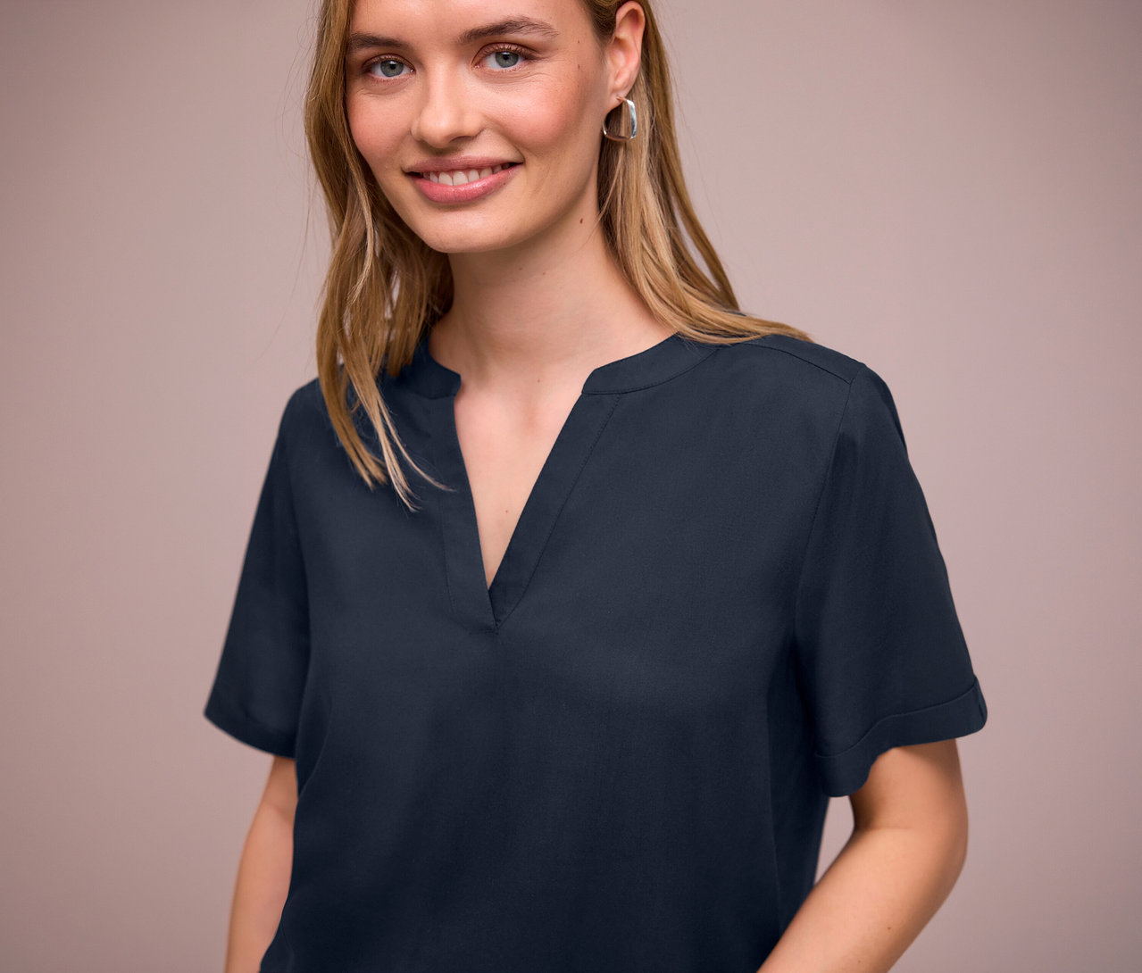 Žena má na sebe tmavomodrú tkanú blúzku Street One s véčkovým výstrihom a strieborné náušnice.