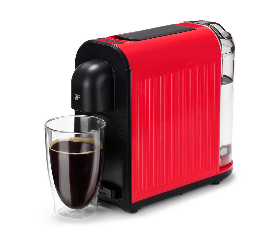 Červený kávovar Cafissimo now red stojí vedľa pohára s tmavou kávou.