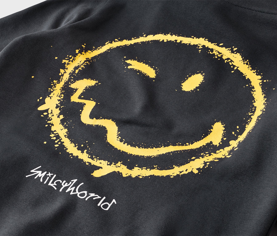 Detail čiernej mikiny s veľkou, žltou, opotrebovanou grafikou smajlíka a bielym nápisom „SMILEYWORLD“ pod ním.