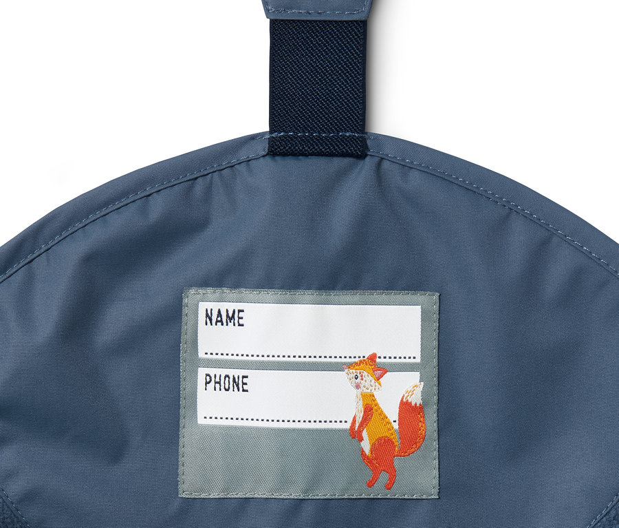 Detail stredne modrých termo nohavíc do dažďa z recyklovaného materiálu s menovkou na meno a telefón a obrázkom líšky.