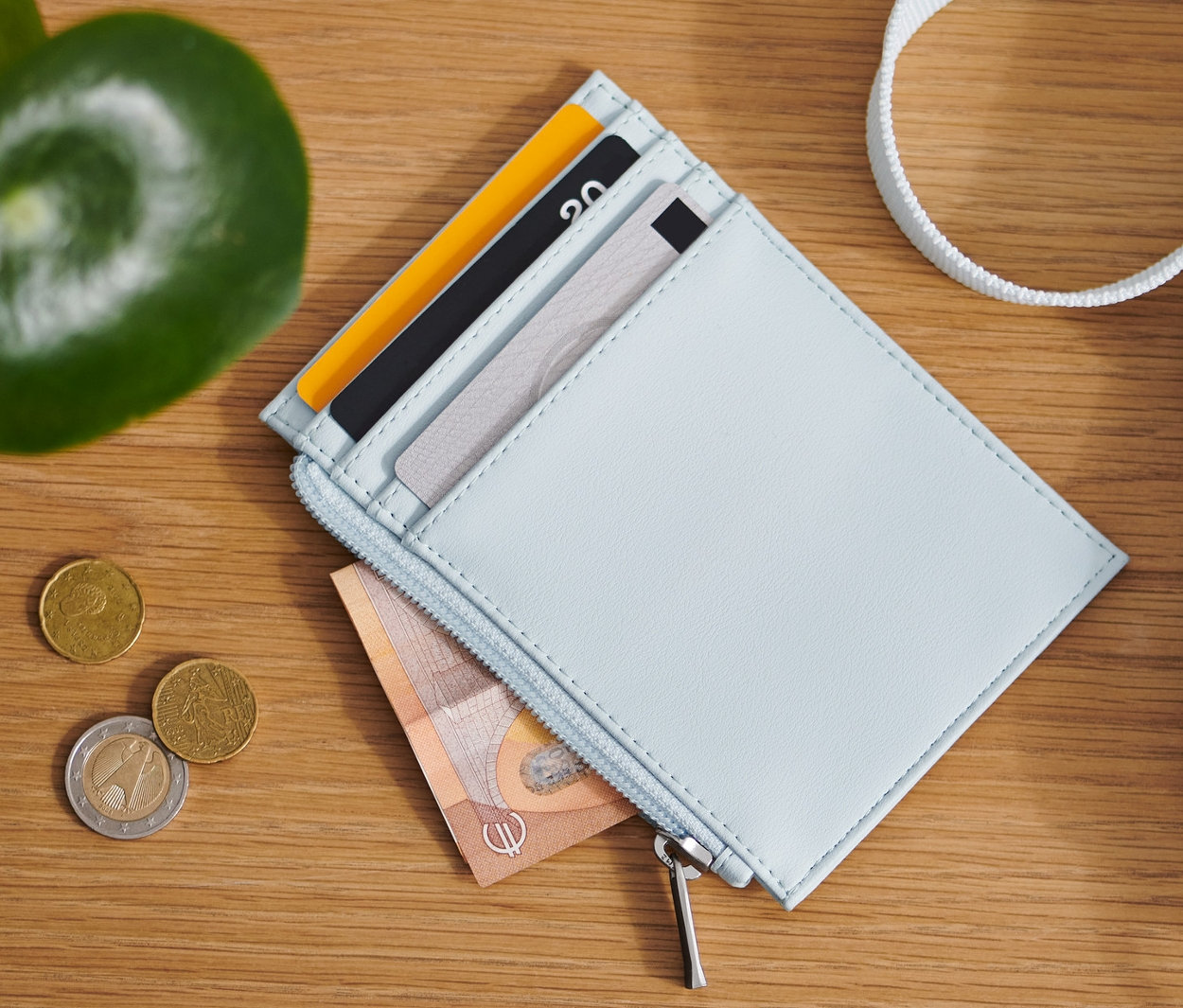 Na drevenom stole leží svetlomodrá peňaženka, mince a taška.