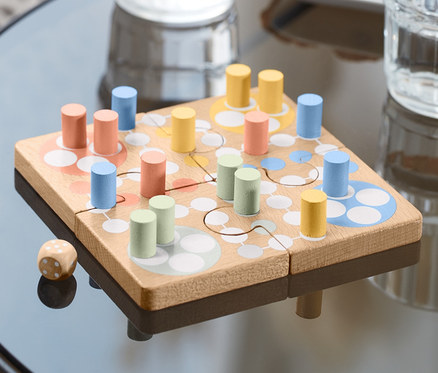 Na stole leží hra Človeče, nehnevaj sa – puzzle s farebnými figúrkami a kockou.