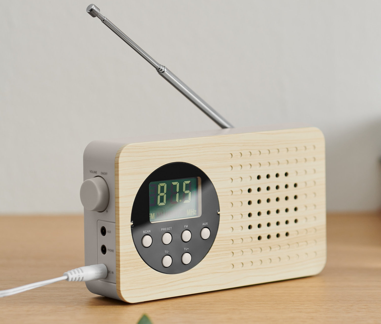 Kompaktné FM rádio s výsuvnou anténou stojí na drevenej skrinke.