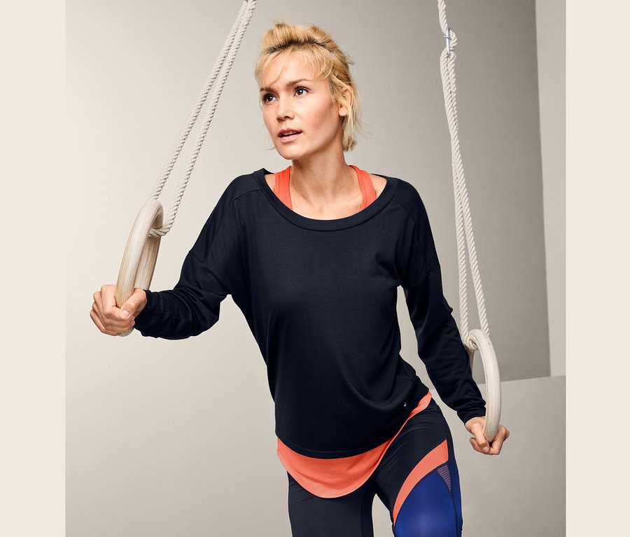 Žena drží gymnastické kruhy a má na sebe športové tričko 2 v 1.