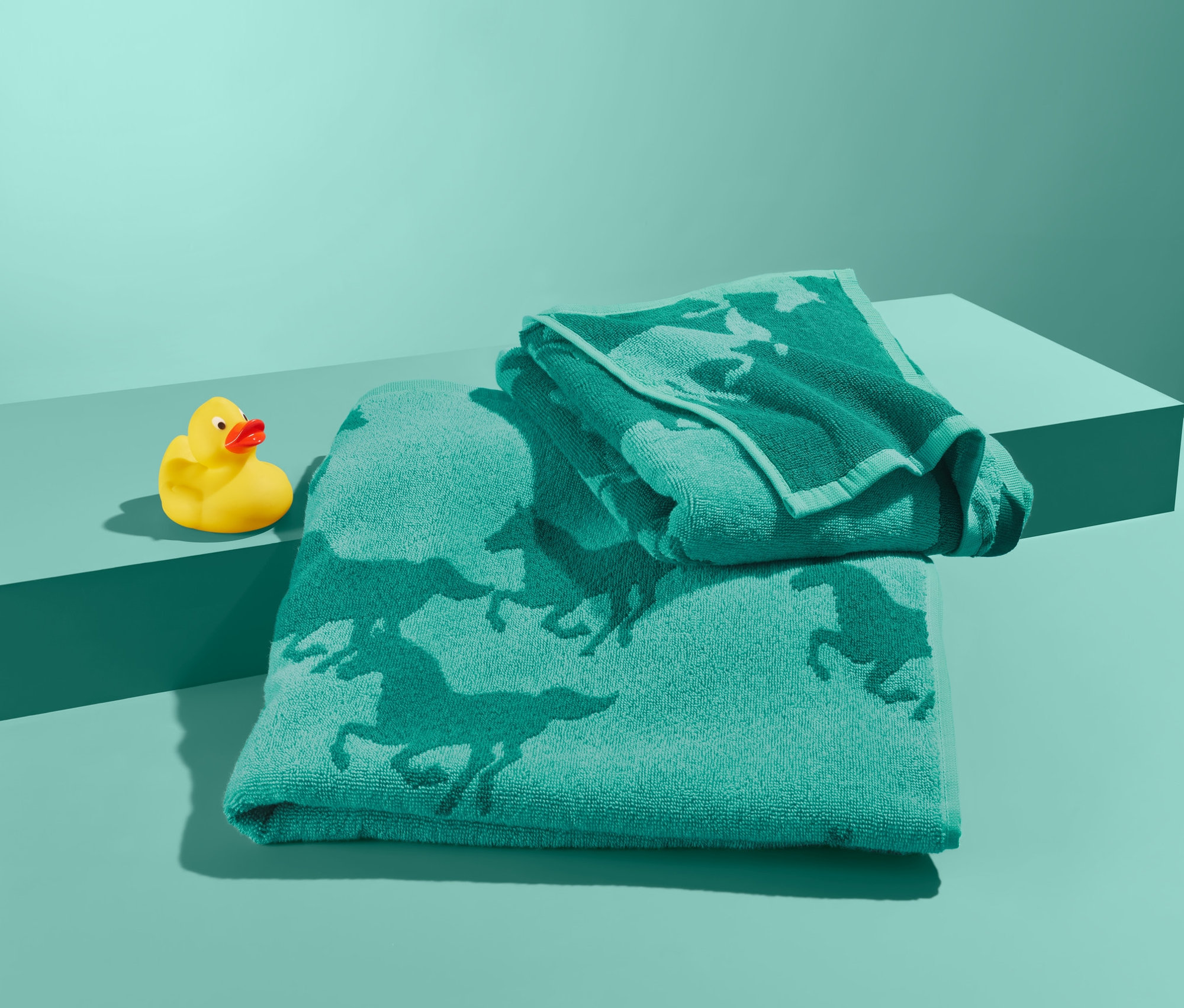 Súprava uterákov s motívom koní a žltá gumová kačička na tyrkysovom pozadí.