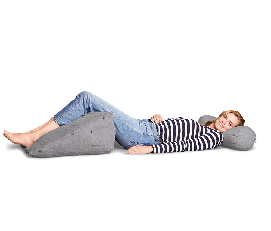 Žena leží na boku a opiera si nohy o sivú podušku na opieranie a hlavu o sivý podhlavník.