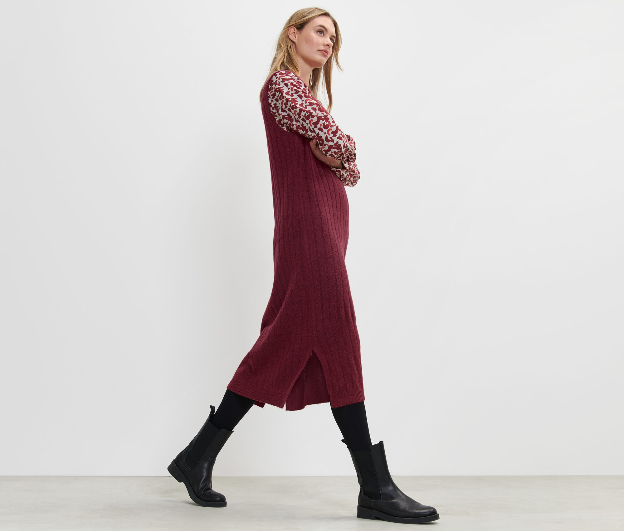 Blondínka kráča a má na sebe červené šaty z rebrovaného úpletu.