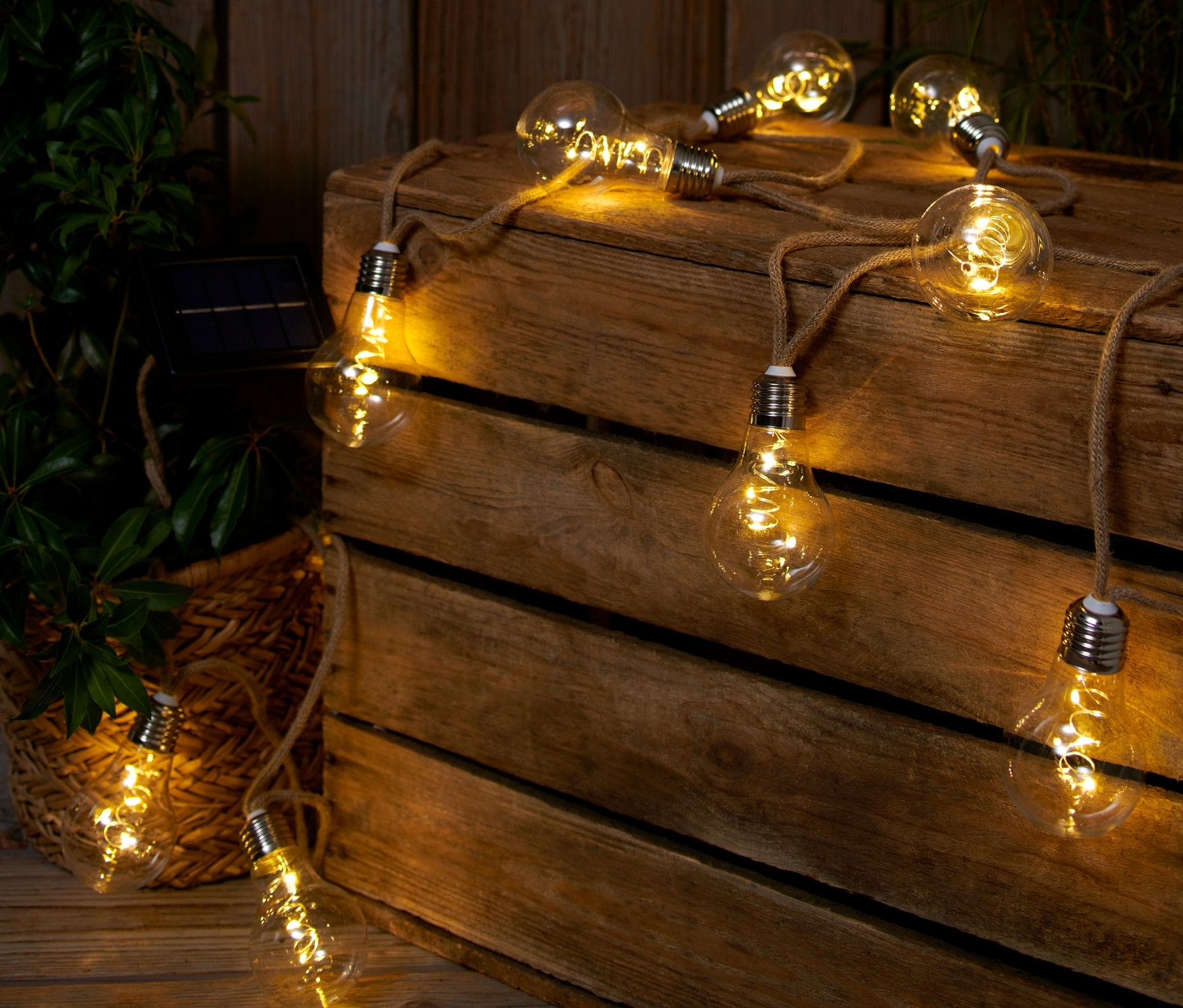 Solárna svetelná reťaz s jutovým lanom leží na drevenej debne vedľa rastliny.