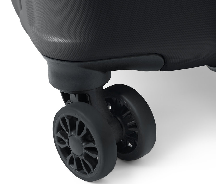 Detail veľkého kufra s tvrdou škrupinou zobrazujúci textúrovaný povrch a dve čierne kolieska.