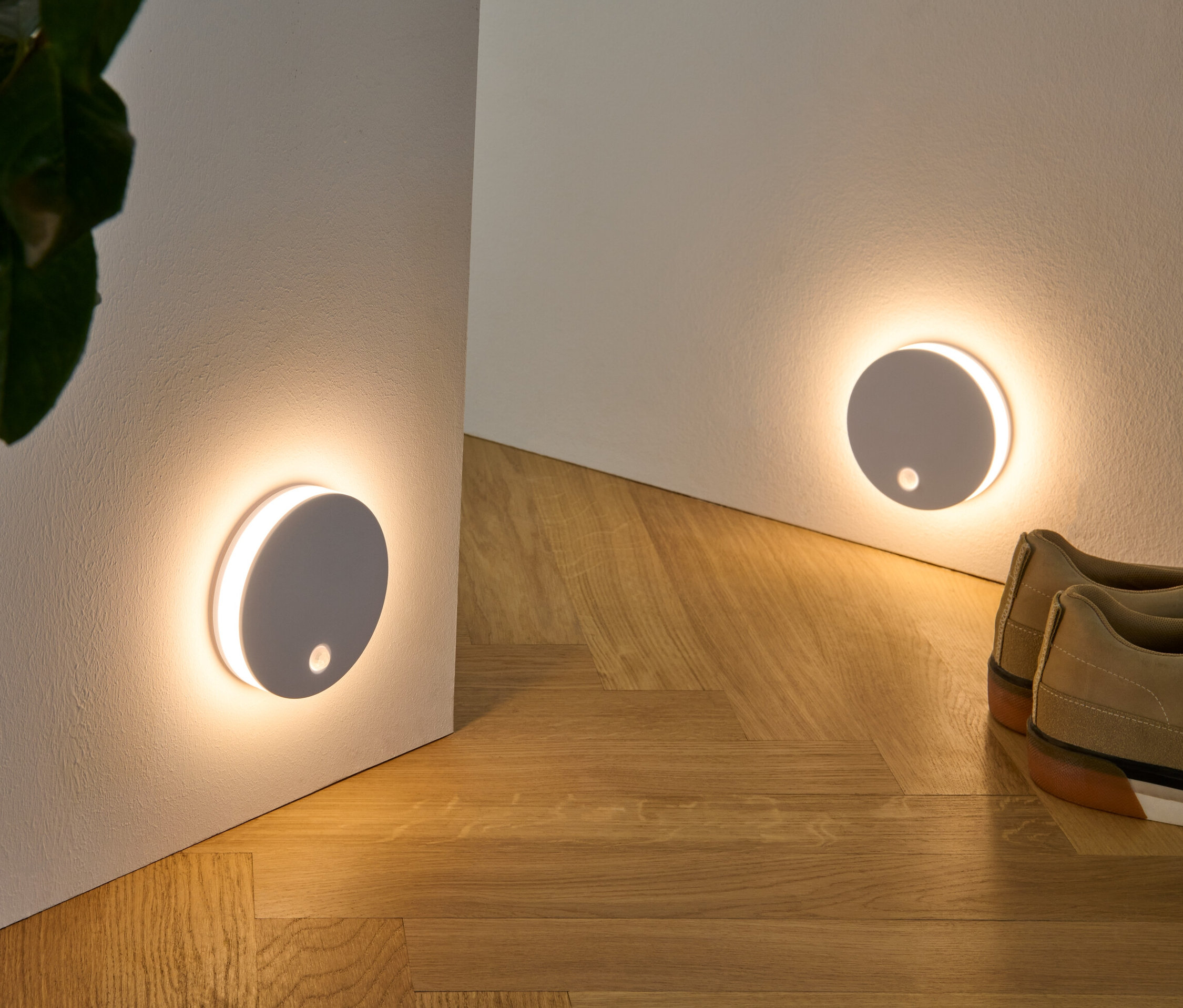 Dve multifunkčné LED svetlá sú pripevnené na stene, spolu s rastlinou v prútenom košíku a topánkami na drevenej podlahe.