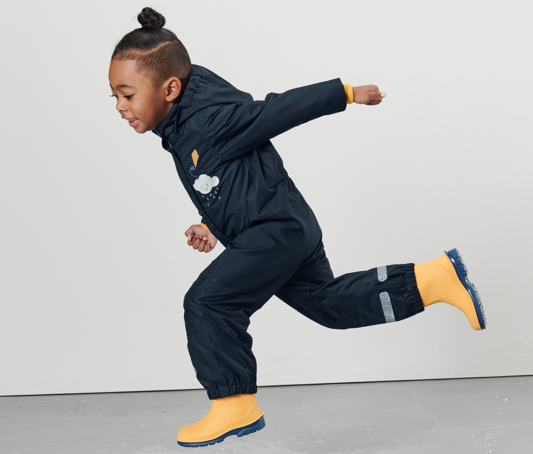 Chlapec v detskom overale do dažďa skáče v kaluži.