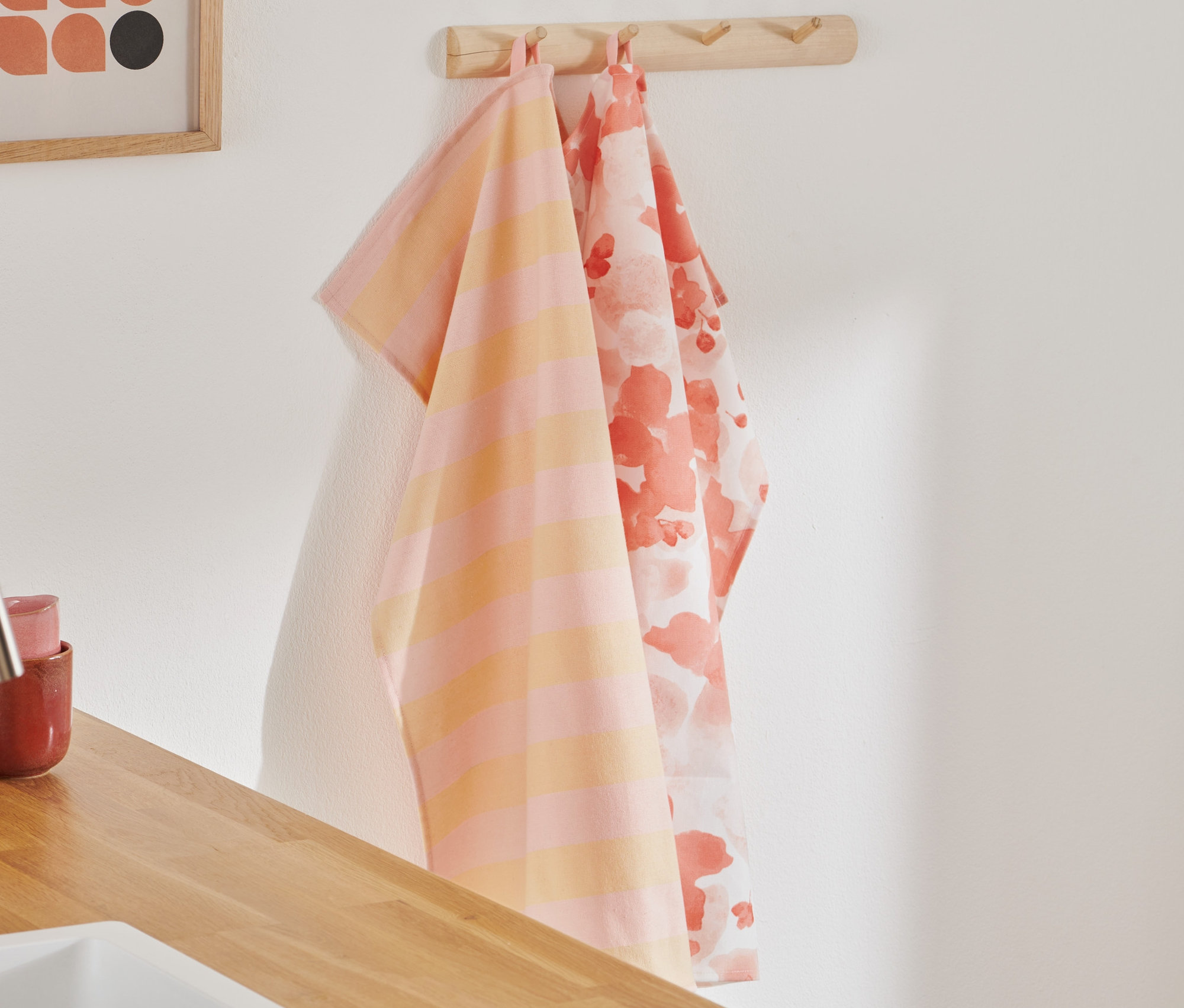 Dve utierky na riad visia na háčiku. Jedna je oranžovo-ružová pruhovaná, druhá má kvetinový vzor.