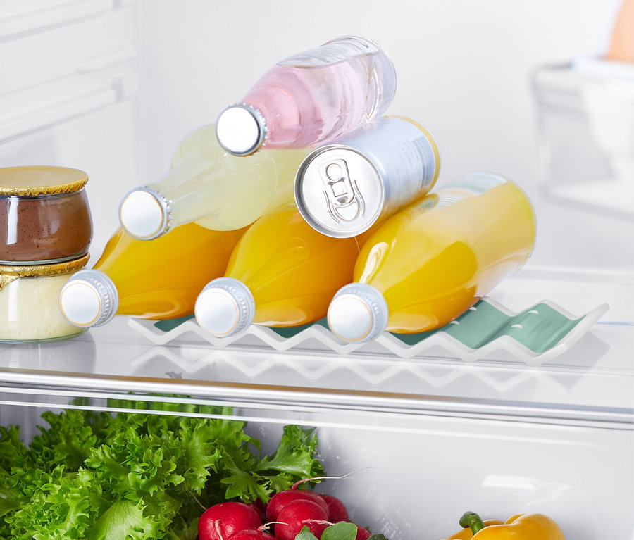V chladničke je držiak na fľaše do chladničky, na ktorom ležia tri fľaše s džúsom a plechovka. V spodnej časti sú vidieť šaláty, reďkovky a žltá paprika.