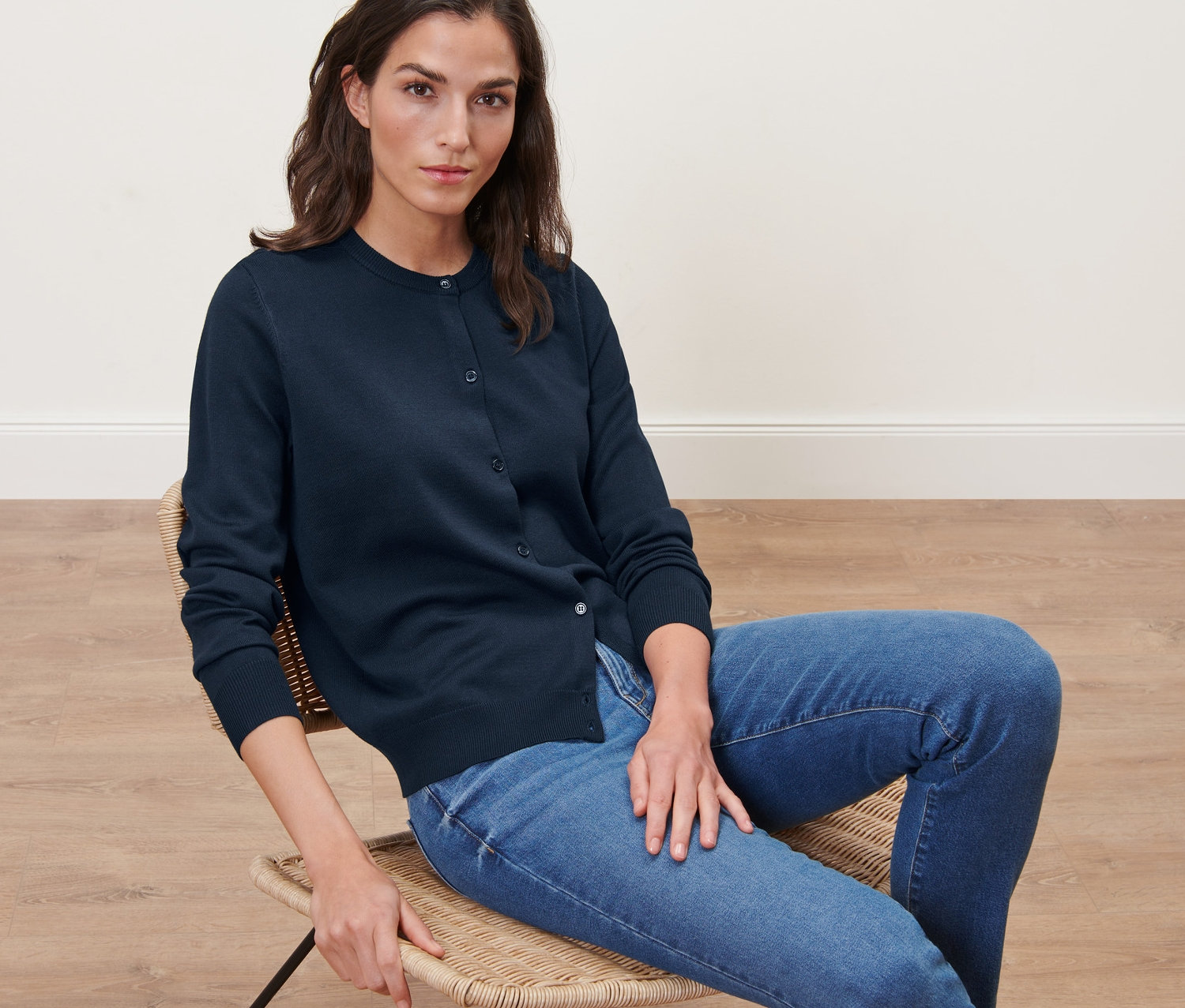 Žena sedí na stoličke a má na sebe modrý kardigán z jemného úpletu.