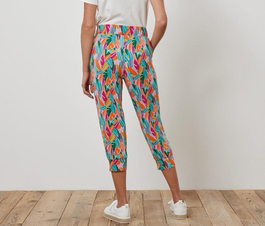 Žena má na sebe 3/4 džersejové nohavice, viacfarebné a biele tenisky.