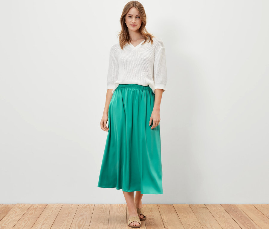 Žena pózuje v bielom tope a zelenej saténovej sukni.