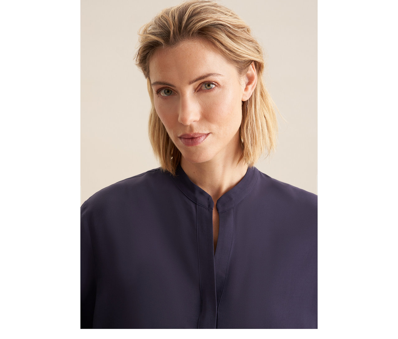 Žena s blond vlasmi má na sebe tmavomodrú tuniku Seidensticker z viskózy so stojačikom a výstrihom do V.