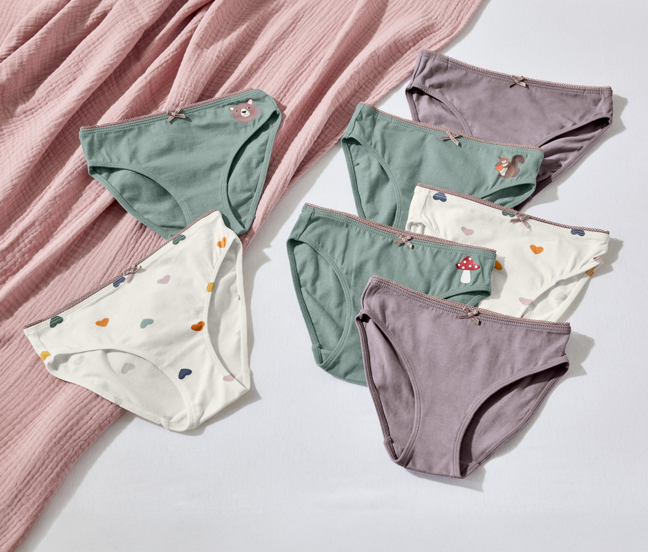 Sedem párov dámskych nohavičiek rôznych farieb a vzorov leží na bielom pozadí vedľa ružovej látky.