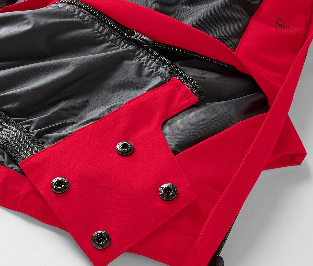 Detail červenej bundy s čiernou podšívkou a patentkami.