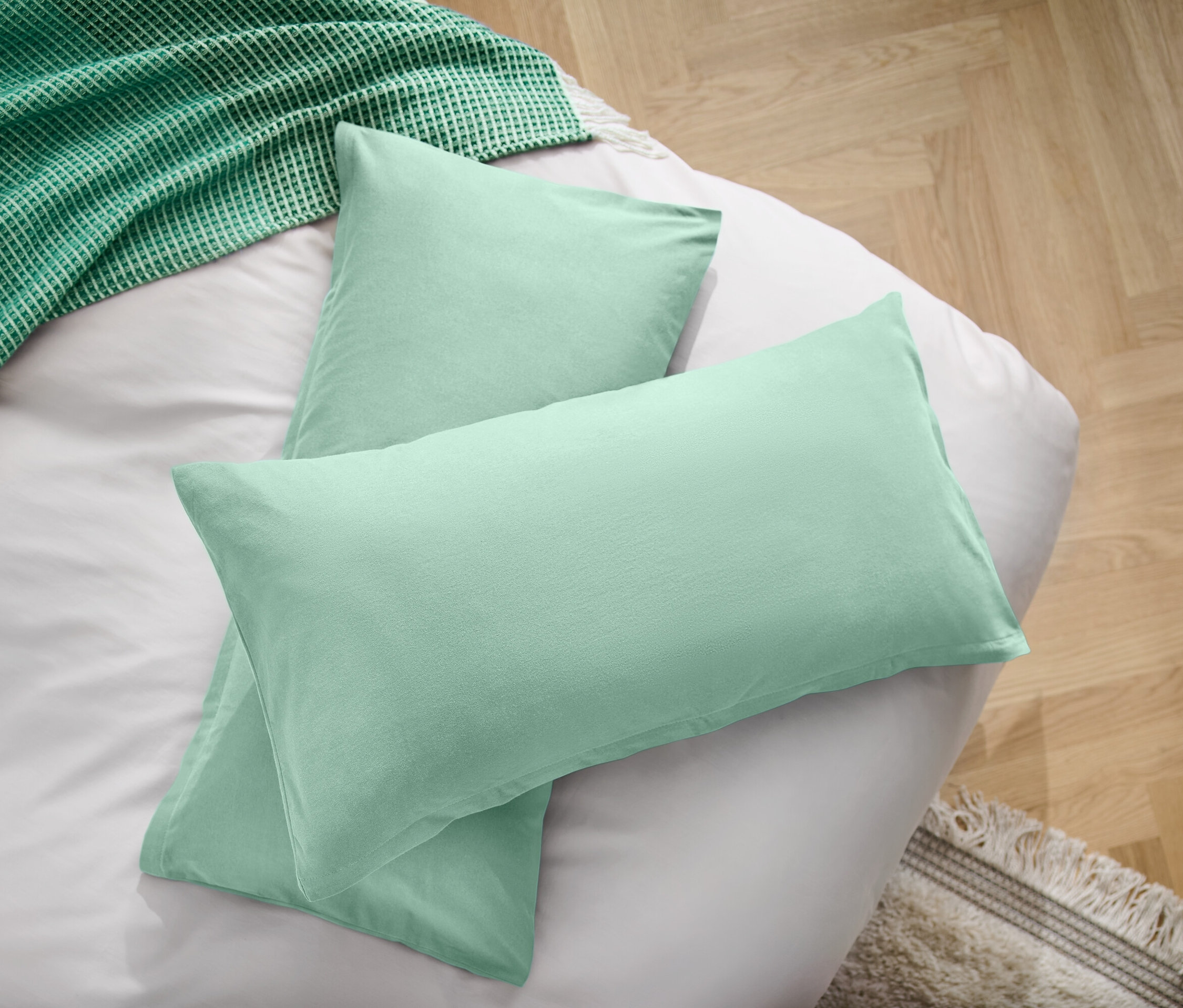 Dva svetlozelené vankúše na bielej plachte vedľa zelenej deky.